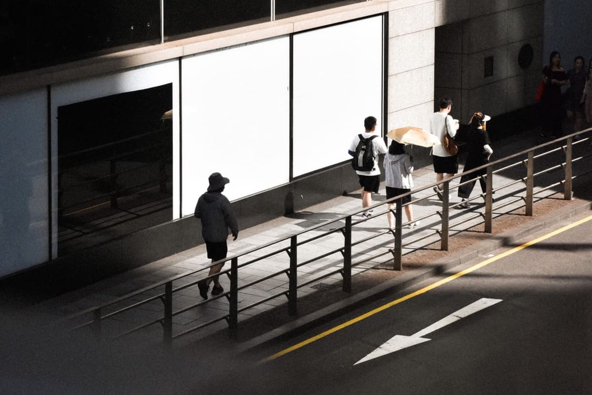 People walking past a building with light and shadow on it.