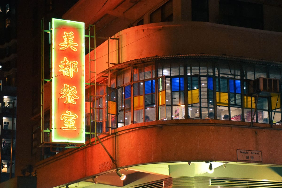 A traditional Chinese calligraphy red and yellow neon sign of a Hong Kong style diner at night