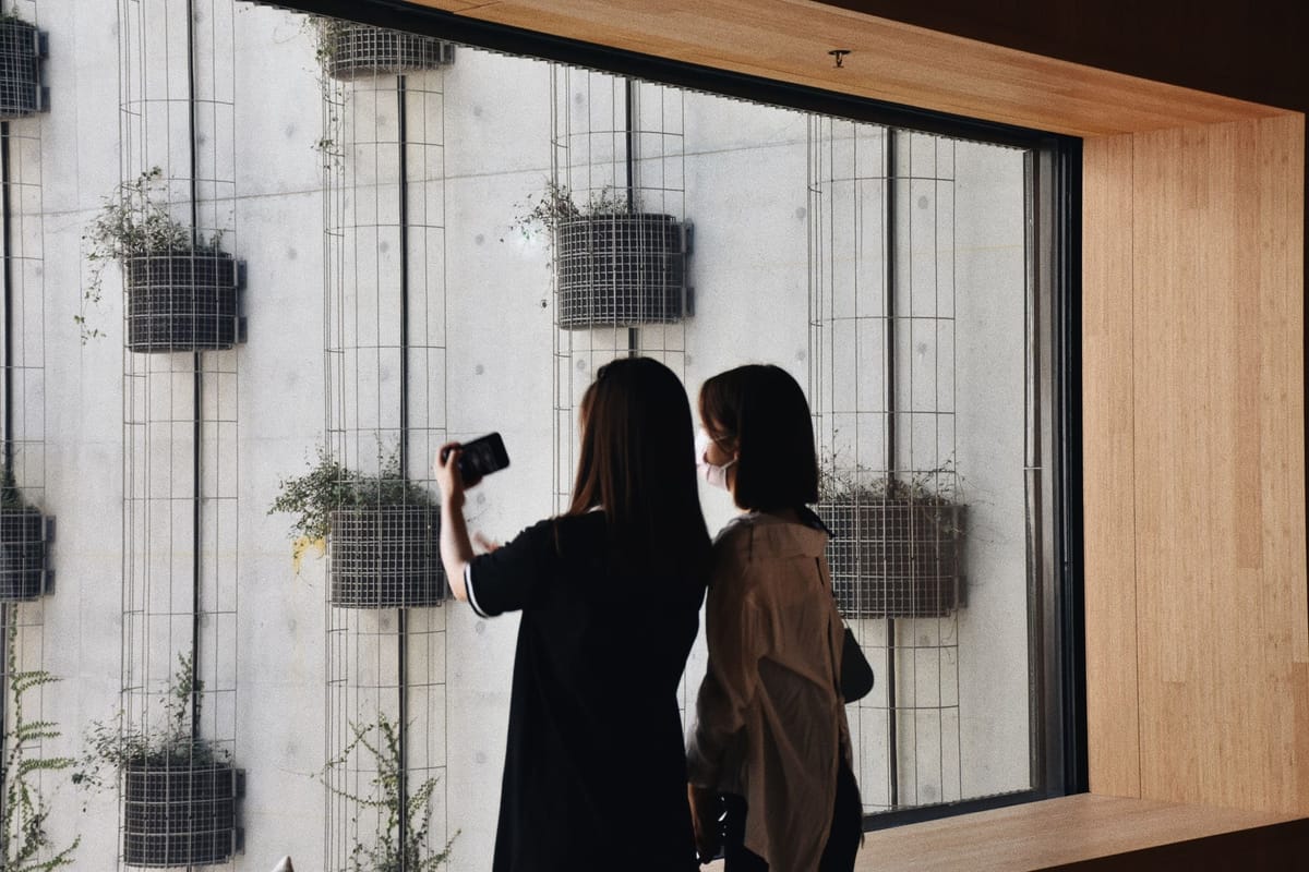 a woman is with her smartphone and her friend, standing near a window of a museum