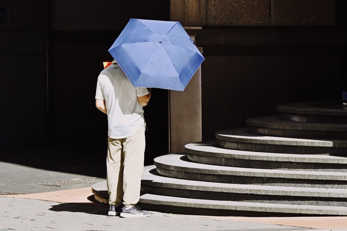 Man with a blue umbrella standing near staircase on a sunny day