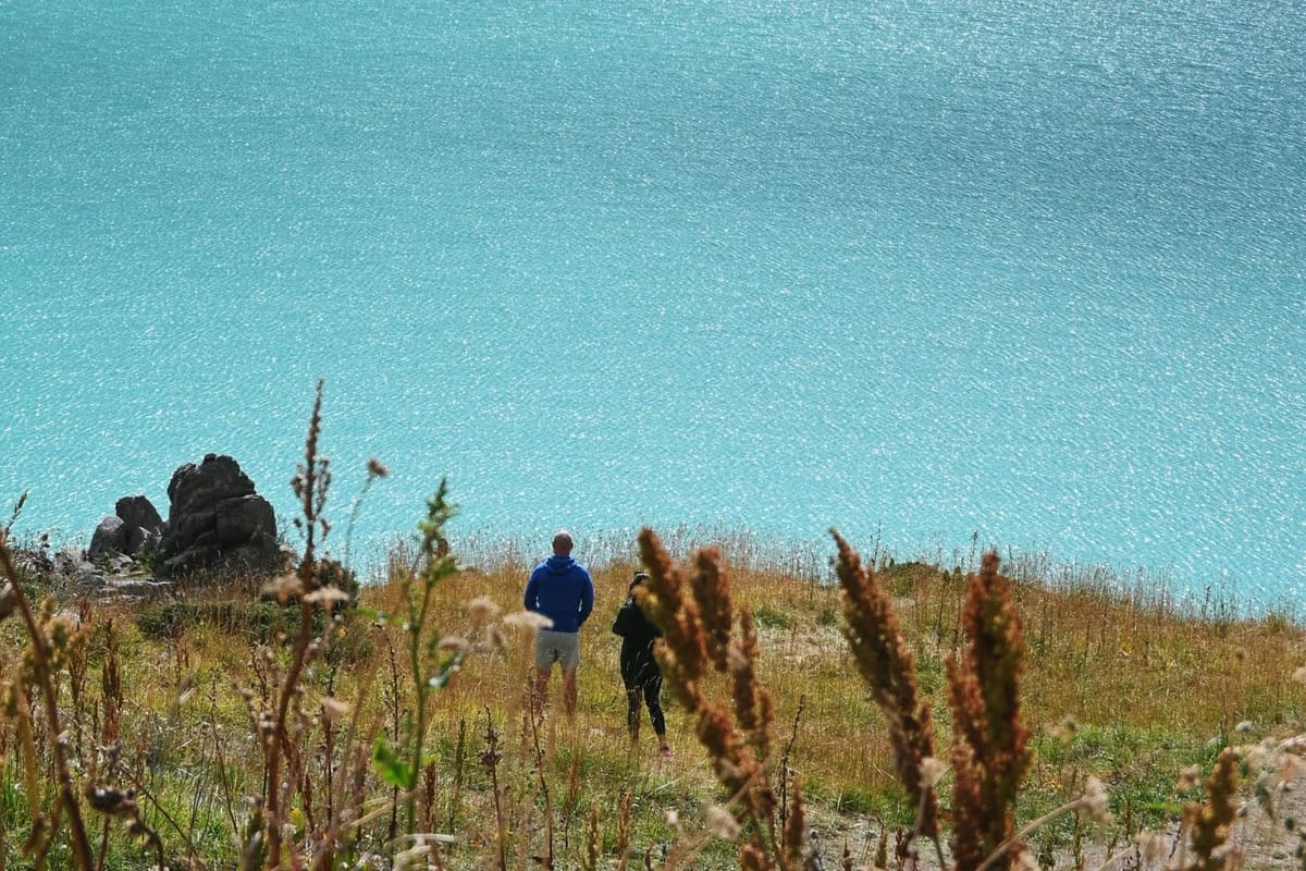 two people stand on grassland and view the turquoise lake